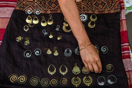 Young womans arm is touching some brass indian jewelry for sale on a black cloth in a festival stand. Different sizes of earrings viewed from aboveの写真素材