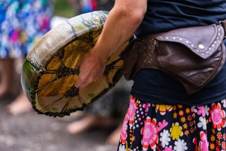 close up on caucasian womans hand holding her sacred drum, new colourful native american leather drum while playing outside with some friendsの写真素材