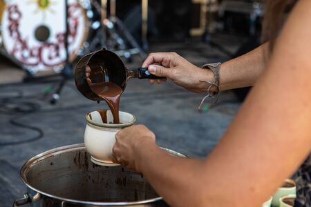 close up on womans hands pouring hot chocolate Drink in the mug, with blurry background of stage and music instrumentsの写真素材