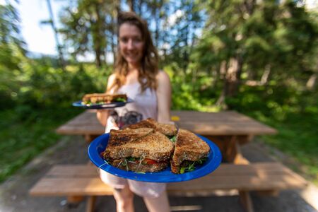 Selective focus of a young adult woman having two plates in her hands with delicious and healthy toast while being in nature environmentの写真素材
