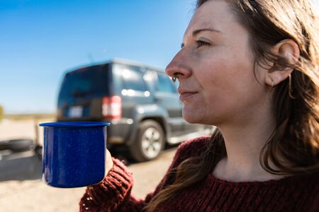 Selective focus of young adult woman holding a cup of coffee or tea while standing outside in front...