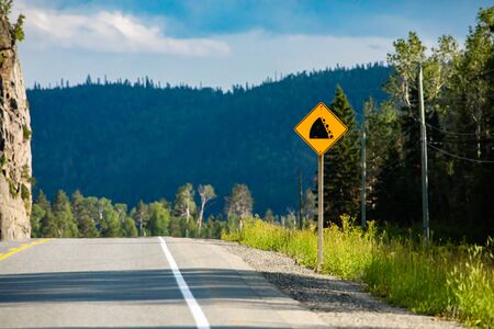 Watch for fallen rock and be prepared to avoid a collision sign. Warning Road Signs on the roadside with pine trees forest backgroundの写真素材