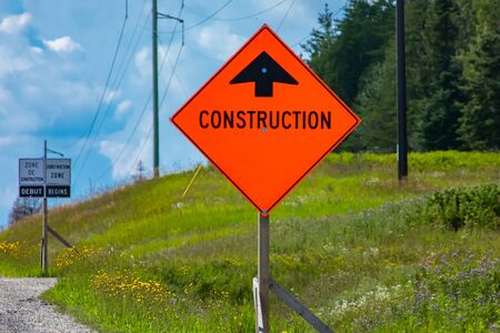 Temporary condition road signs, Construction work. on Canadian rural country roadside with pine trees background, close up warning orange symbolの写真素材