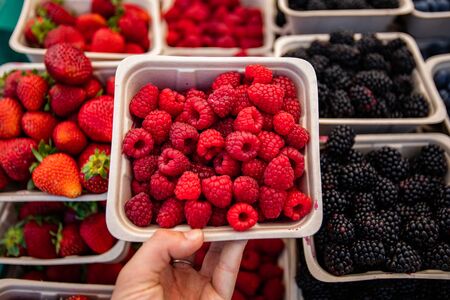 A first person and top down shot during a harvest fair as a shopper picks a carton of juicy raspberries from a stall の写真素材