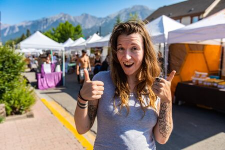 Portrait of a caucasian girl with brunette hair and tattooed arms, giving double thumb sign of approval during a local street fair with copy spaceの写真素材