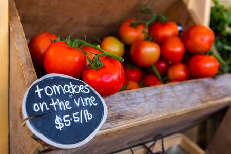 A close up view of a price sign advertising ripe tomatoes on the vine, on a market stall during a...