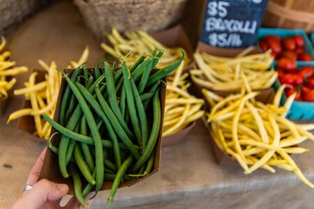 Cartons of organically grown runner beans are seen from the top and closeup as a person picks vegetables at a food fair during summerの写真素材