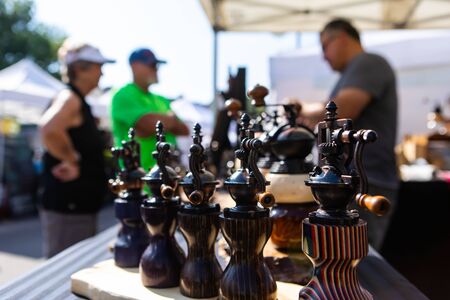 Selective focus shot of vintage handmade salt and pepper grinders for sale at a local market, blurry people are seen shopping in backgroundの写真素材