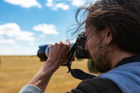 Young male photographer with long hair shooting the horizon with a professional DSLR camera and a...