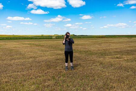 Young female photographer with long hair taking pictures outdoor in a rural environment in a bright sunny day. Copy space on top. の写真素材