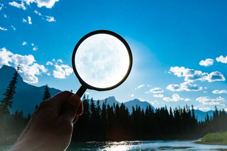 man holding a magnifying glass over a bright blue sky with scattered clouds during summer in nature with copy spaceの写真素材