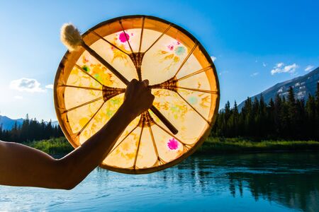 A close up shot on the arm of a spiritual person holding a mystical native drum against nature, used...