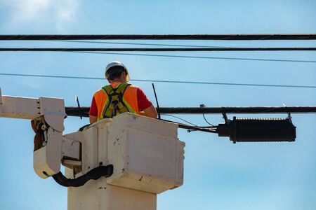 A low angle and close up shot of a man at work in an aerial work platform, AWP, wearing high visibility safety clothing and a hard hat making repairsの写真素材