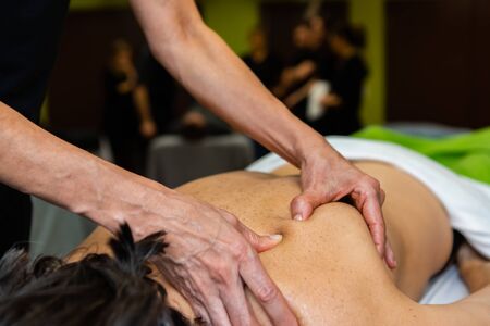 A close up view on the hands of a masseuse giving a Swedish back massage, practicing kneading technique during training session, with blurry pupilsの写真素材