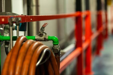 green metallic pipe with industrial water valve and orange tube selective focus close up, modern brewhouse brewery beer factory interior viewの写真素材