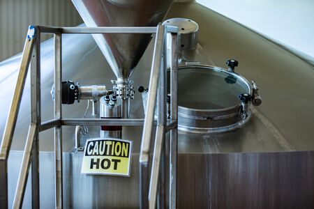 Mash lauter tun vessel close up, Brewing tank top with stairs, round glass manway door, caution hot...