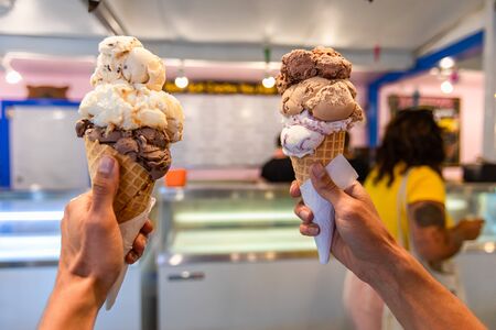 A close up and first person perspective of a man holding two waffles cone with scoops of ice cream...