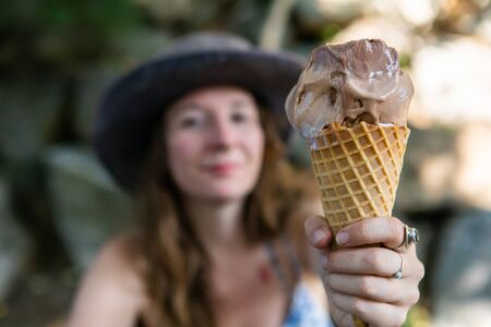 A closeup and point of view perspective of an ice cream cone. being held by a confident woman out of...