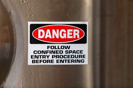 DANGER, FOLLOW CONFINED ENTRY PROCEDURE BEFORE ENTERING, warning vinyl sticker sign on stainless steel cold industrial tank, with copy spaceの写真素材