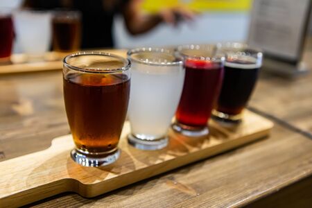 Flight of craft four of different beers glasses, brown black white and red beer on a wooden tray...