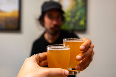 two beer glasses cheering close up selective focus point of view, a caucasian man wearing black hat...