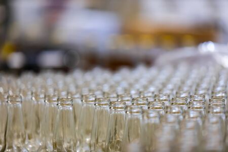 a lot of new white glass empty beer bottles top, selective focus close up view with blurred copy space, conveyor belt craft brewery factory microbreweryの写真素材