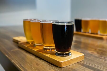 Flight of craft four of different beers glasses with black beer on a wooden tray. during a tasting...