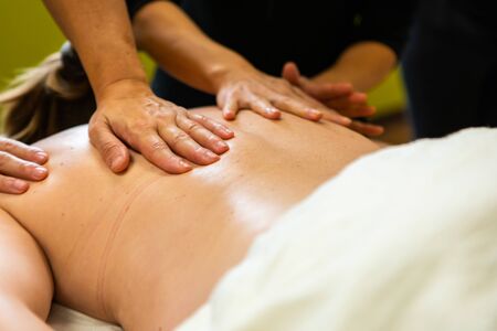 A close up and low down view as two people massage the back and shoulder of a lady during professional skills course, with copy space to rightの写真素材