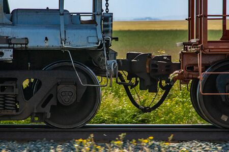 Close up of train coupler connecting two wagons of a Canadian freight or cargo train. Green fields and blue sky in the background.の写真素材