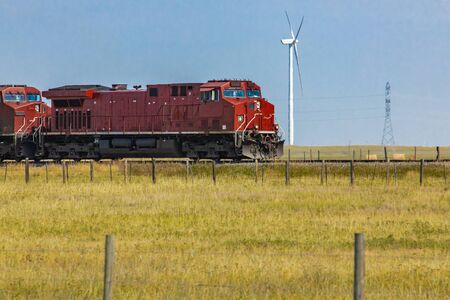 Wide angle shot of bright red vintage locomotive of a red Canadian National Railways. Moving towards right. Wind turbine in the background.の写真素材