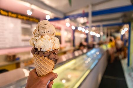 A close up and first person perspective of a man holding a waffle cone with scoops of ice cream at a shop, with blurry counter in the backgroundの写真素材
