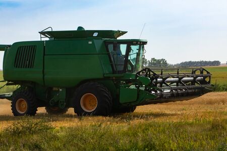 A close up and side view of a large green combine harvester, details of the cutter bar, reel and thresher unit, designed to harvest grain copsの写真素材
