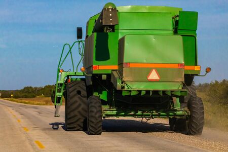 A large green combine harvester is seen from behind, parked on a country road. Caution sign and high visibility strip warn of slow moving vehicleの写真素材
