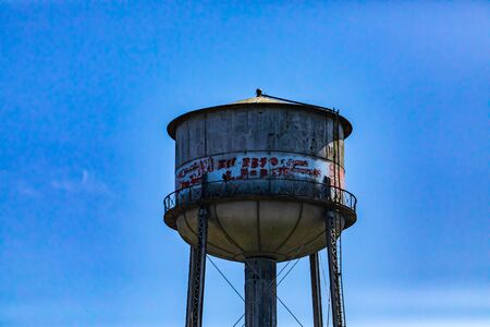 Architectural details of an old water storage tank tower. Weathered in a state of disrepair, covered in graffiti. Against a blue sky with copy spaceの写真素材