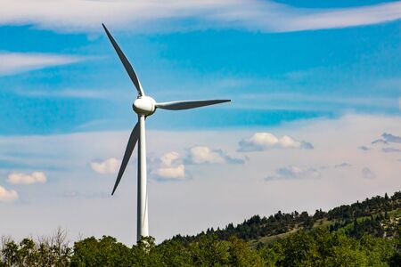 A single wind turbine is seen in rural Alberta, Canada. Against a blue sky with scattered clouds. Farming of kinetic energy as a renewable powerの写真素材