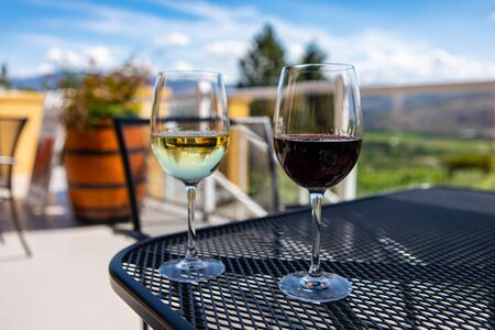 a couple of glasses of white and red wine on the table in selective focus. close up view against patio terrace with green vineyard landscape backgroundの写真素材