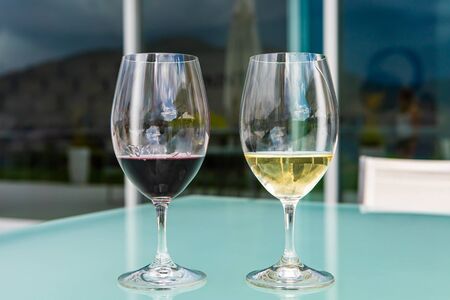 pair of glasses on glass table close up, selective focus view, two wine glasses filled of dark red and golden white wines, winery luxury tasting roomの写真素材