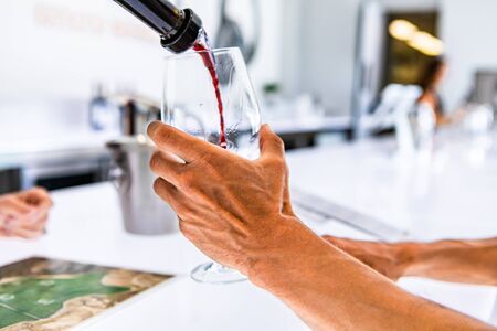 red wine pouring from the bottle to the customer wineglass selective focus, close up, isolated, fresh colors with bar white led lights backgroundの写真素材