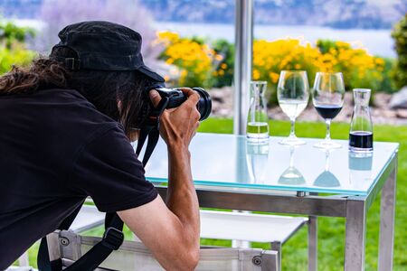man photographer with long hair wearing black rear back view as he takes photos of wine glasses with a professional DSLR camera, wine winery conceptの写真素材
