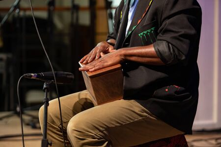 Midsection of african man wearing black blazer and playing music on wooden box in front of...