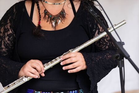 Closeup midsection of fashionable woman wearing black top and necklace while holding flute by microphone stand against wallの写真素材