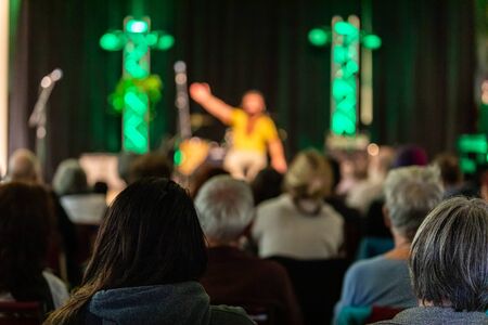 Rear view of audience enjoying and listening male artist telling story on stage against curtain in...