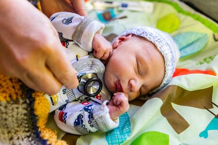 First health checks of new born baby boy, seen close up as obstetrician uses stethoscope to monitor health of days old infant in colorful blanketsの写真素材