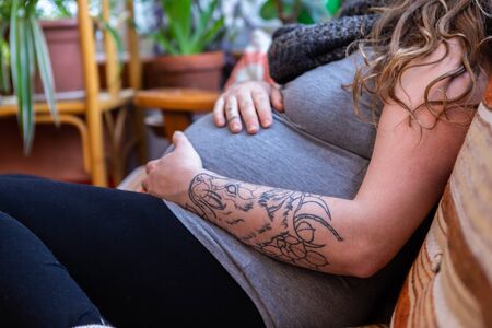 A close up shot of a heavily pregnant woman in the third trimester relaxing on sofa in family room,...