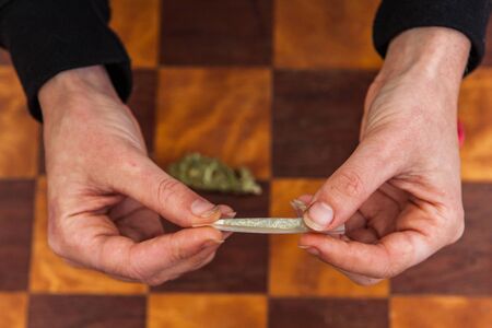Closeup shot of hands twisting a ground cannabis filled rolling paper completing the rolling process of making a joint. Weed bud on the table below.の写真素材