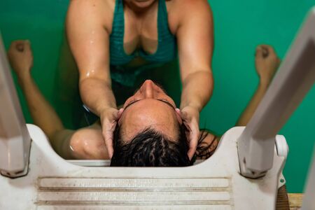 High angle close-up view of female therapist hand giving water massage on head to young man. leaning...