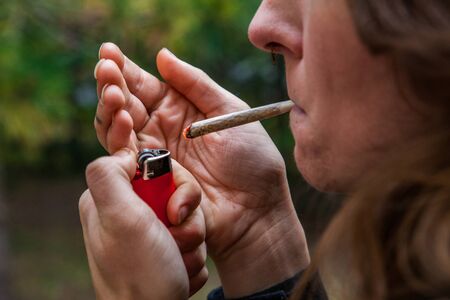 Closeup cropped shot of caucasian womans face with hand rolled marijuana joint held in her lips...