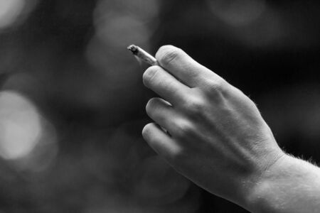 Black and white selective focus closeup shot of caucasian womans hand holding marijuana joint....