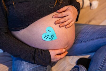 A creative gender reveal message is seen on the big belly of a pregnant woman, heart shaped slogan says its a boy as she rests hands on baby bumpの写真素材