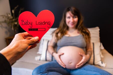 First person perspective as expectant father holds a red heart with message baby loading, blurry...